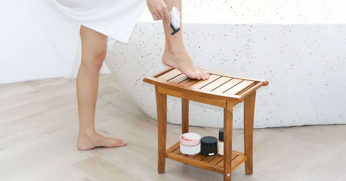 2-tier acacia wood shower stool with shelf in a bathroom holding shampoo and body wash