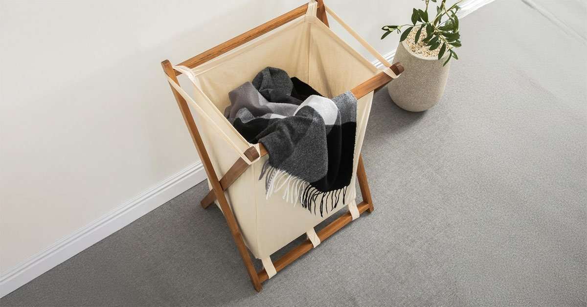Acacia laundry hamper folded flat showing slim storage profile behind a door