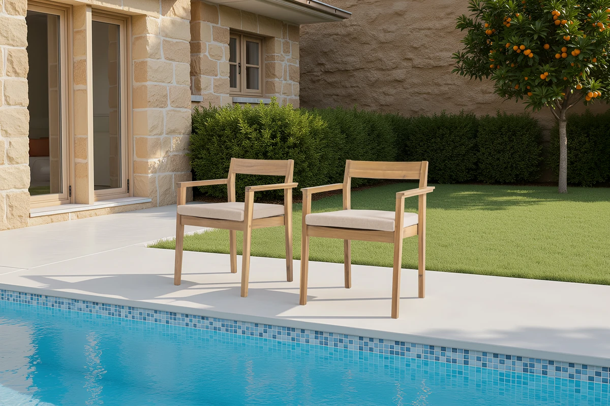 Two cushioned acacia wood patio chairs in a landscaped outdoor setting