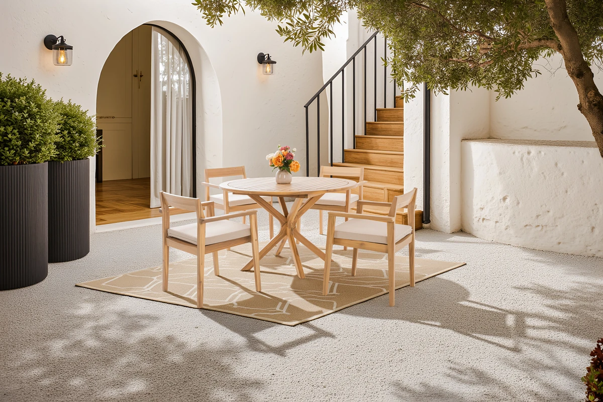 Round acacia dining table with four cushioned chairs in an outdoor courtyard